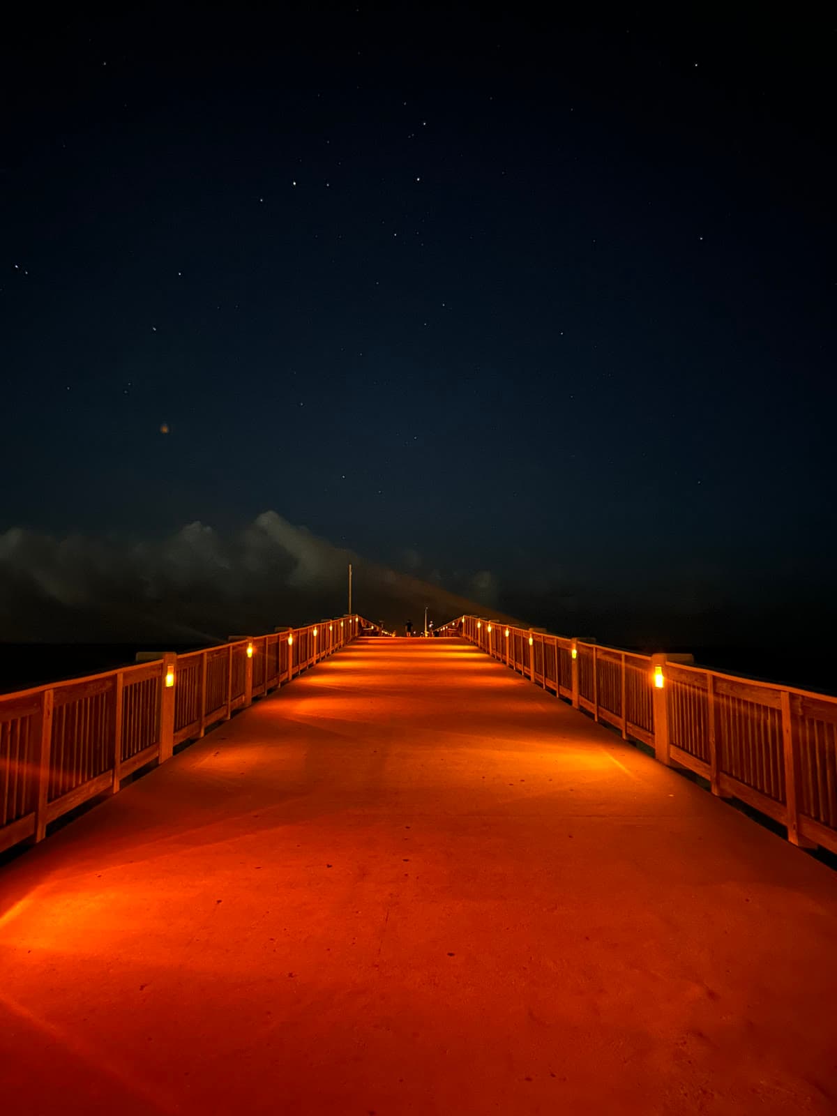 A lit wooden pier stretching out under a starry night sky