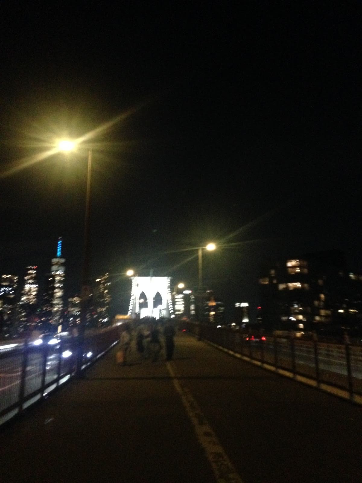 Walking the Brooklyn Bridge at night toward the lit tower
