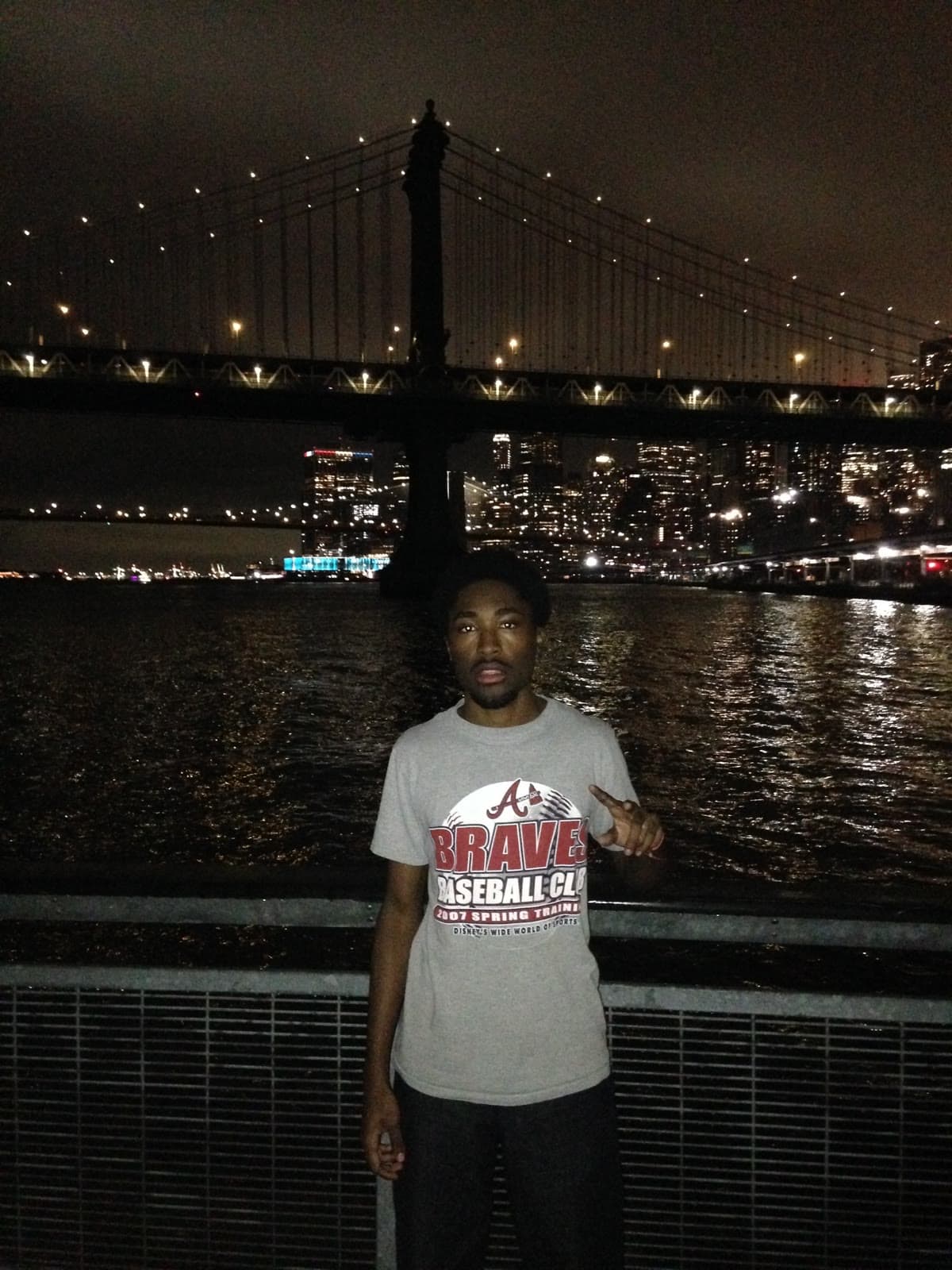 Standing by the East River at night with the Manhattan Bridge behind