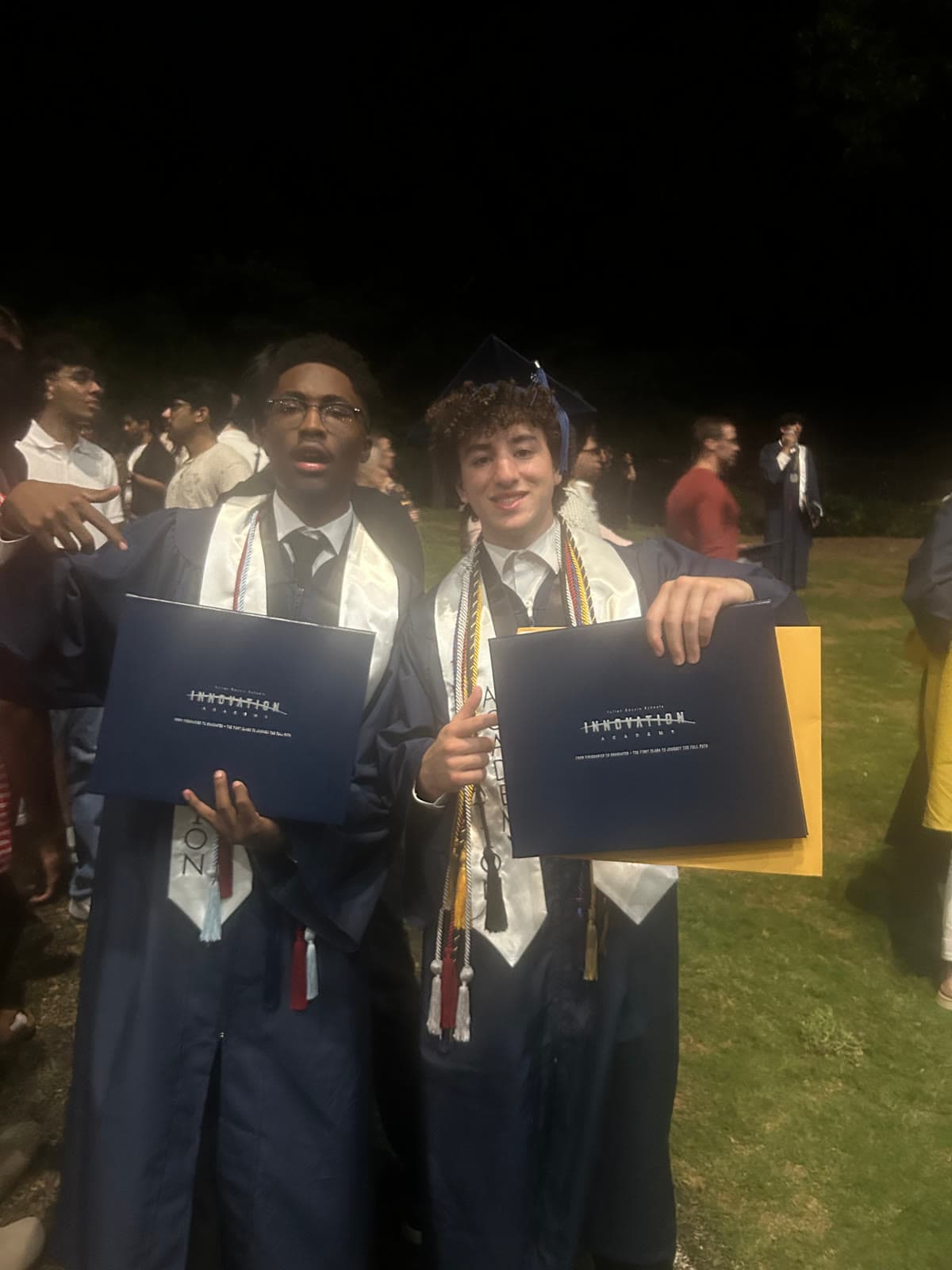 Two graduates holding up their diplomas at night
