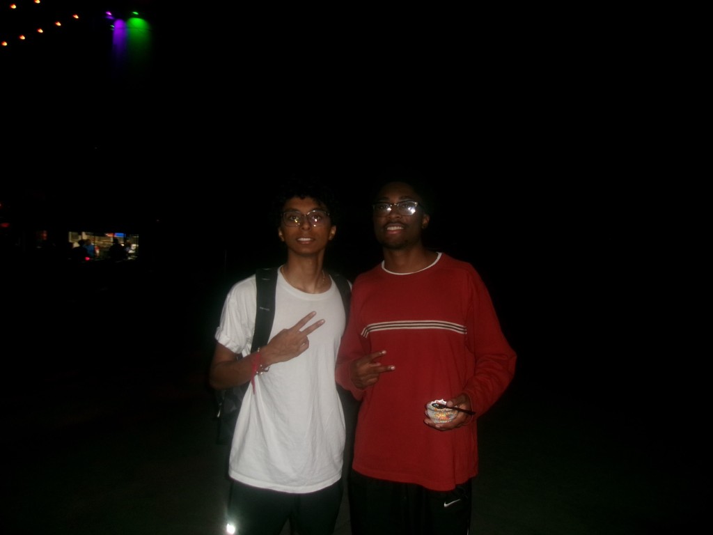 Two friends at night, one making a peace sign