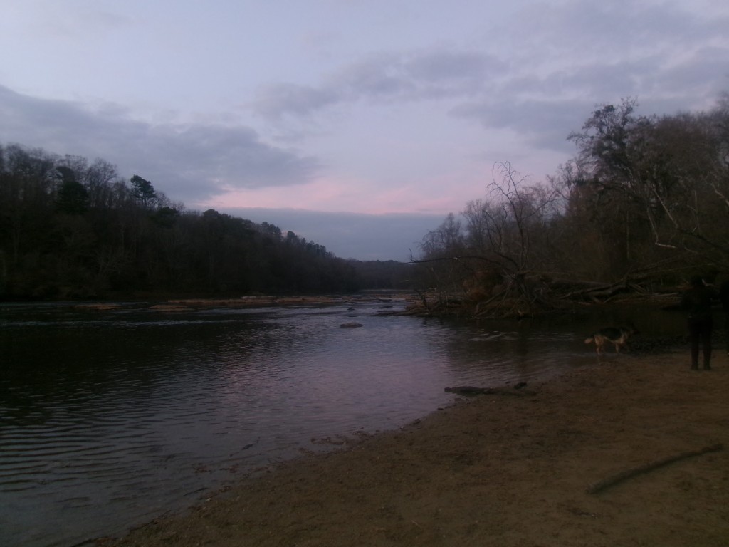 River at dusk with forested banks; person and dog on the shore